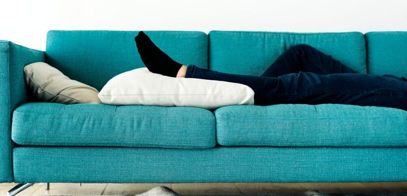 Sédentarité : Personne allongée sur son canapé, le pied sur le coussin. 